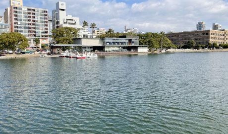 福岡市にある大濠公園で、大きな池の周囲はジョギング、ウオーキングができる歩道があります。中央にはレストランがあり、その左側には貸しボートが何艘か湖面に浮かんでいます。