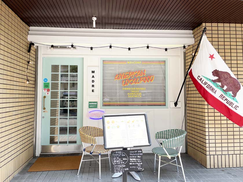 西公園のアメリカ料理店MADRE マドレの外観です。お店の前に机と椅子があり、Calofornia Republicとかかれた旗が飾られています。お店の窓にはAMERICAN LOCAL FOODとかかれています