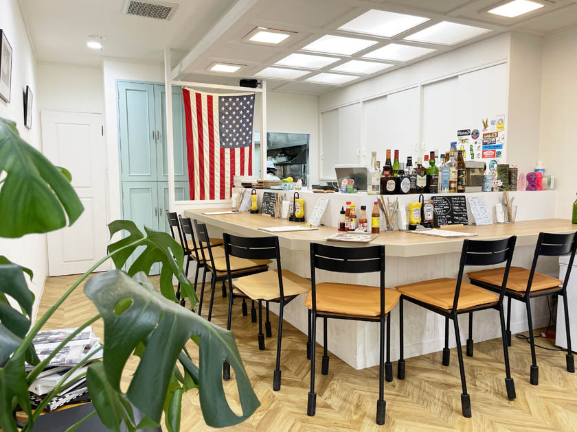西公園のアメリカ料理店MADRE マドレの店内です。カウンターに椅子がならんでいます。奥にはアメリカの国旗である星条旗が飾られています